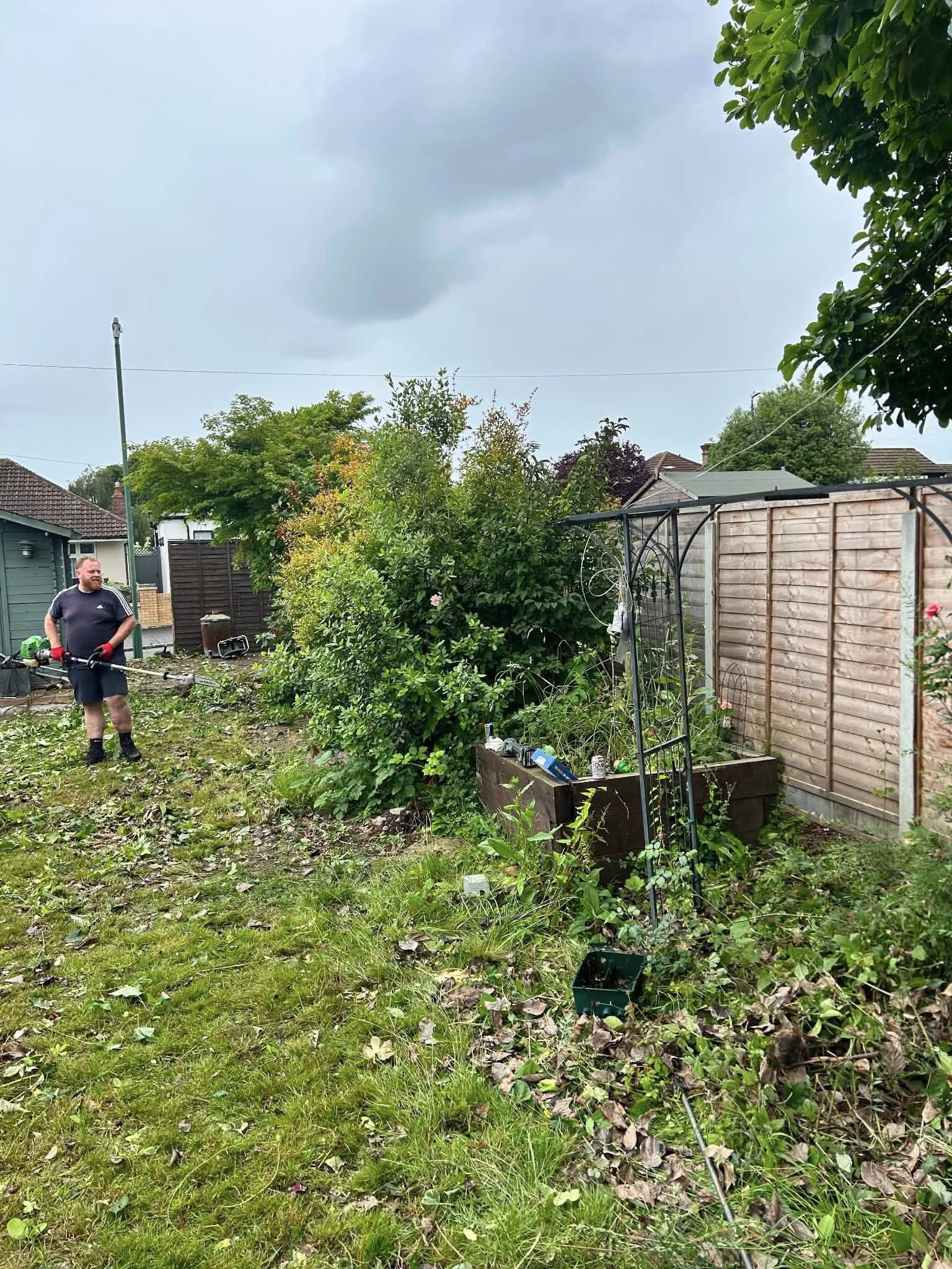 Before: overgrown garden with weeds, plants and wooden fence