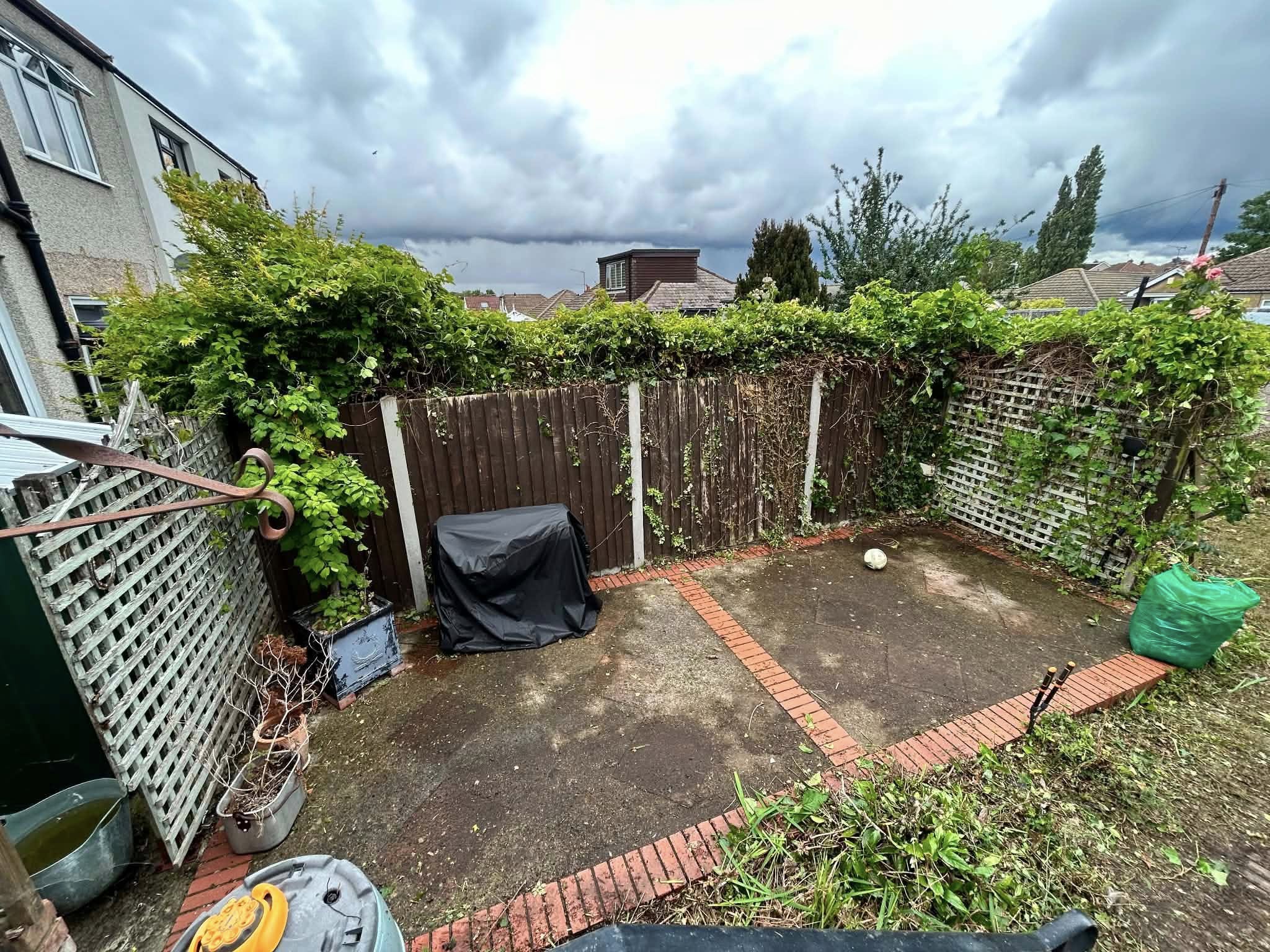 Before: overgrown residential garden with fencing and covered items